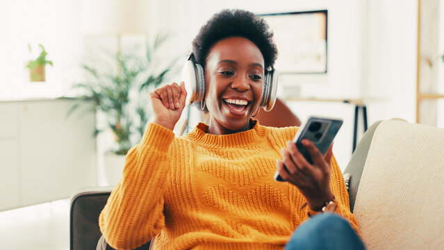 Black woman, phone and headphones on sofa in home, music and relax with sound in living room. African person, smartphone and listening with audio, streaming and subscription on mobile app at house