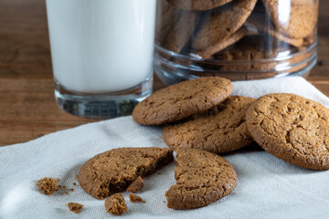Ginger snap cookies on cloth with glass of milk and cookie jar in background.