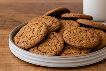 plate of ginger snaps on wooden table. Glass of milk in background.
