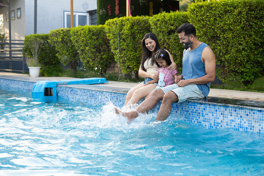 Young indian parents and little child daughter enjoy splashing water at swimming pool in summer holiday, India Family having fun relaxing together at hotel resort vacation. Bonding and togetherness