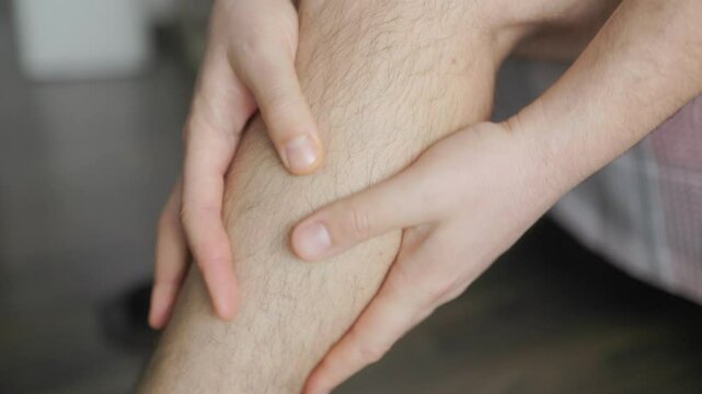 Man rubbing leg due to pain or fatigue, close-up of hands and hairy lower leg