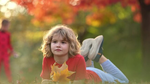 Autumn fall child mood. Little child in autumn orange leaves, outdoor portrait. Funny child face with autumn leaves in autumn park. Child playing with falling golden leaves. Portrait of kids dream.