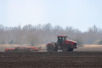 Fototapeta premium A tractor cultivates the soil in a field in spring, mid-April