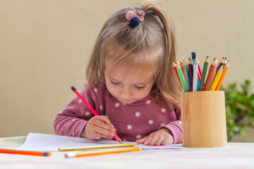Focused preschool girl is concentrating on drawing with colored pencils, demonstrating early childhood development, creativity, and learning through playful exploration at home