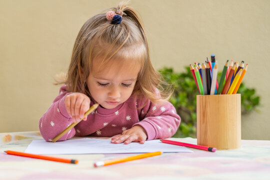 Focused young girl is developing her creativity and fine motor skills by drawing with colored pencils, highlighting the importance of early childhood education and exploration