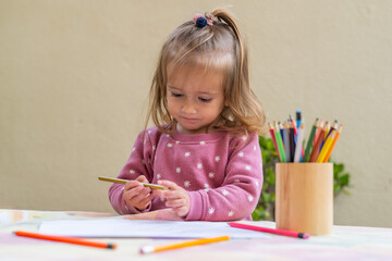 Young girl, around two years old, engaging in a drawing activity with colored pencils at a table,...