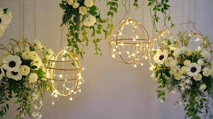 Elegant flower arrangements with hanging geometric spheres illuminated by fairy lights, against a neutral background - Powered by Adobe