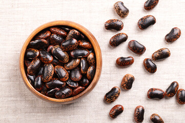 Scarlet Runner beans in a wooden bowl on linen fabric. Dried, raw seeds of large and speckled...