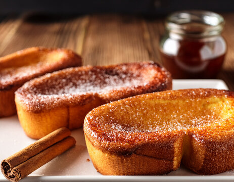 Deliciosas torrijjas dulce tradicional de semana santa con pan con unas ramitas de canela y az&uacute;car por encima, fritas en aceite sobre un plato en una mesa de madera
