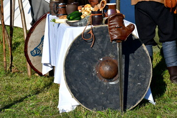 A close up on a set of medieval or Scandinavian shields located next to a glove, a sharp sword and a table full of medieval meals and drinks seen in summer during a historic fair in Poland
