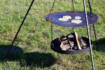 A close up on several short breads or other medieval cookies made on a metal bowl attached to some prongs and with hot logs and planks located below to ensure a proper temperature during cooking