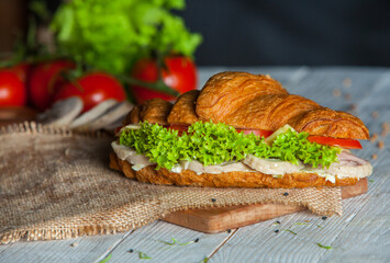 Croissant sandwiche with salmon and green parsley. Croissants with red fish on wooden cutting board. Healthy breakfast. Appetizer. Starter meal