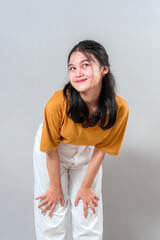 Young Asian woman showing a shy and playful expression while bending forward slightly. Her face...