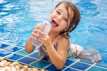 Happy child drinks water from bottle in pool
