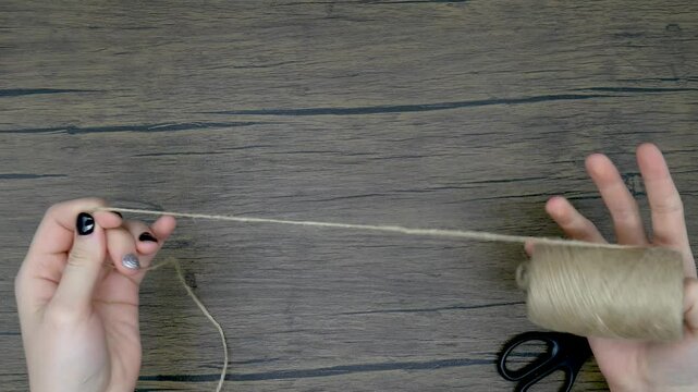 Women's hands unwind a string from a spool and cut a piece with scissors. Diy craft concept.