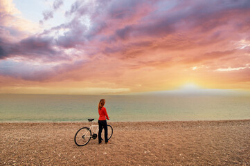 Fototapeta premium Woman Admiring Scenic Beach Sunset with Bicycle in Beautiful Setting..