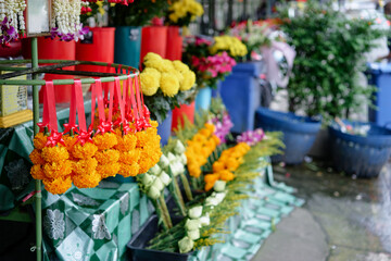 Fototapeta premium Vibrant marigold garlands and assorted floral arrangements are showcased at a bustling outdoor asian flower market. The display evokes cultural significance for events and rituals.