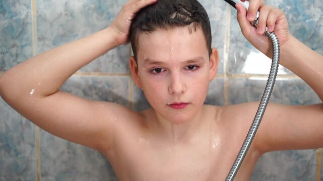 Teenage boy bathing under a shower with a flexible hose. Washes off foam and dirt. Close-up.