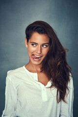 Fototapeta premium Funny face, tongue and comedy of woman, silly and confident by backdrop, hair and casual fashion. Happy female person, beauty and emoji or goofy, care and joke or pose, comedy and gray background
