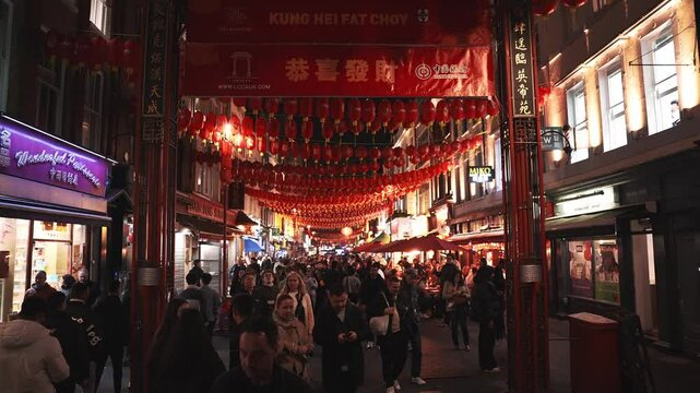 Crowds walk through London's Chinatown at night under red lanterns and a banner reading Kung Hei Fat Choy, celebrating Chinese New Year.