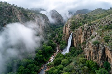 Breathtaking valley vista featuring a stunning waterfall cascading down a rocky cliff, partially obscured by misty clouds.