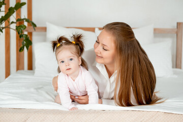 a mother with a baby daughter, a mother gently hugs her baby girl kissing, maternal love and care, a happy family with a baby on the bed at home in the bedroom.