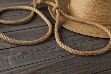 Lasso made of cotton rope and straw hat on wooden background, closeup