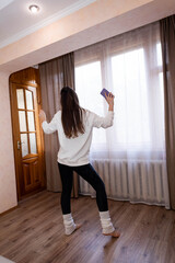 Happy, energetic girl in a white sweatshirt and black leggings dancing at home