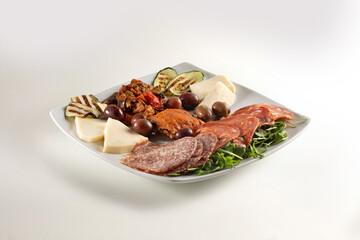 Appetizer of cured meats, rocket, cheese, zucchini and olives on a white background.