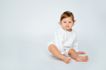 Fototapeta premium A baby boy on a white isolated background with a place for text is sitting in white knitted clothes. A small happy child in a winter sweater , space for text