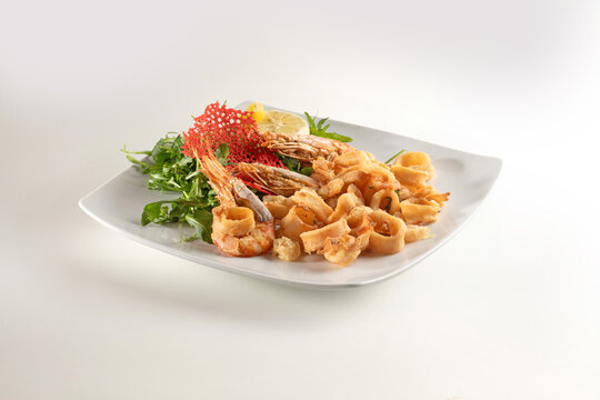 mixed fried fish served with green salad and lemon on a white plate. Dish on a white background.