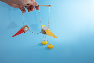 Bird marionette toy made of cardboard tube, paper beak, wings, plastic bottle cap feet, and string....