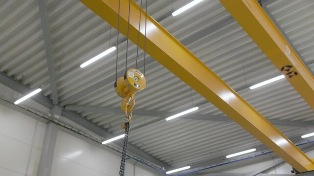An industrial yellow overhead crane with a blue hoist system is suspended from steel beams, ready for heavy lifting operations in a clean, modern manufacturing facility