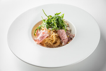 A plate of pasta is topped with slices of ham, fresh arugula, and grated cheese. The dish exemplifies a stylish and delicious approach to Italian cuisine, perfect for any dining occasion.