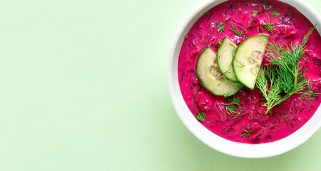 Cold summer beetroot soup in bowl over green background