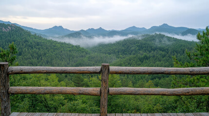 Fototapeta premium Breathtaking view of misty mountains and lush greenery from wooden terrace at dawn