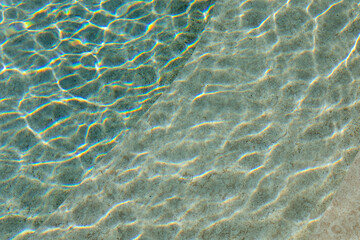 A close-up view of clear pool water, with gentle ripples and soft reflections, creating a peaceful atmosphere. The sunlight dances on the surface, highlighting the tranquil beauty of the water