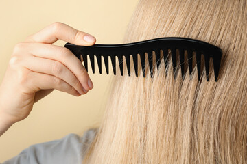 Obraz premium Woman brushing hair with plastic comb on beige background, closeup