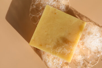Soap bar with foam on peach background, top view