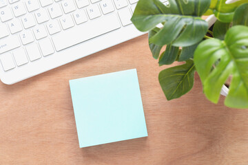 Top view, The sticky notes are light blue color and plants in pots, keyboard on a wooden workplace. Blank space for text and template for your message...