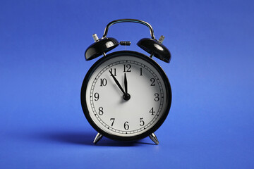 One black alarm clock on blue background