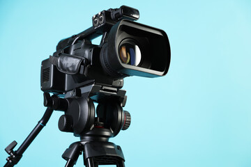 Modern video camera on light blue background, closeup. Space for text