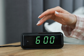 Woman turning off digital alarm clock on bedside table indoors, closeup