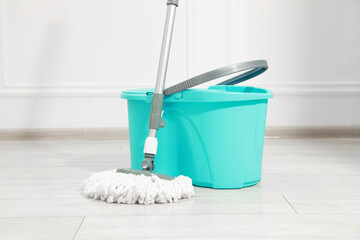 String mop and bucket on wooden floor near white wall