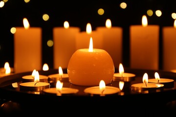Many burning candles on dark surface, closeup