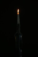 One burning candle in bottle on black background