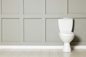 Ceramic toilet bowl near grey wall indoors