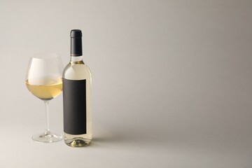 Tasty white wine in glass and bottle on light grey background, space for text