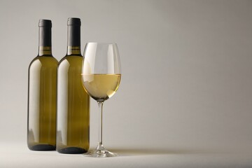 Tasty white wine in glass and bottles on light grey background, space for text