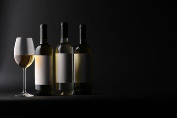 Tasty wine in glass and bottles on black background, space for text